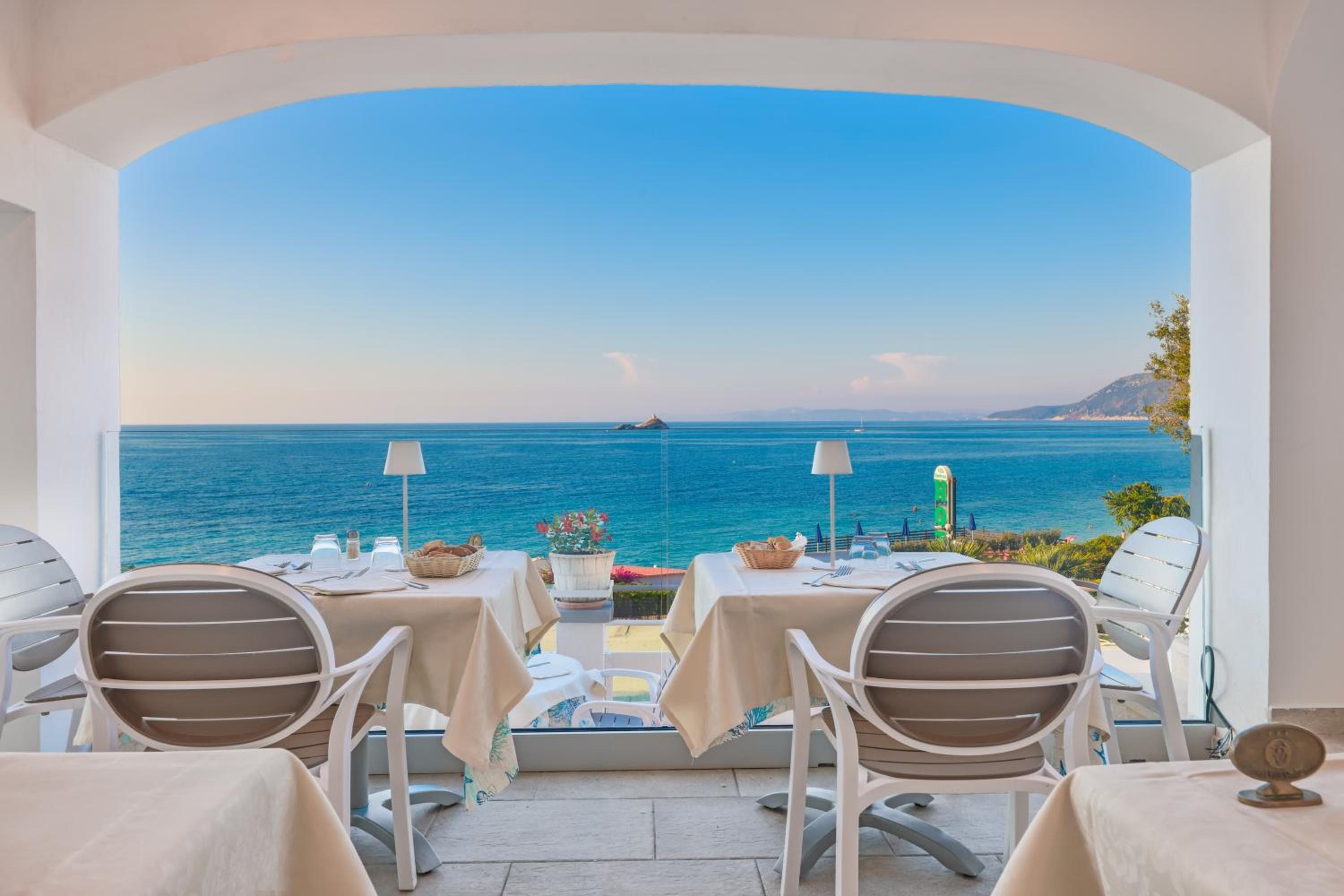 A terrace with tables and chairs overlooking a sea view.