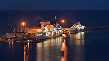 Una grande nave da crociera ormeggiata in un porto, con edifici industriali sullo sfondo.