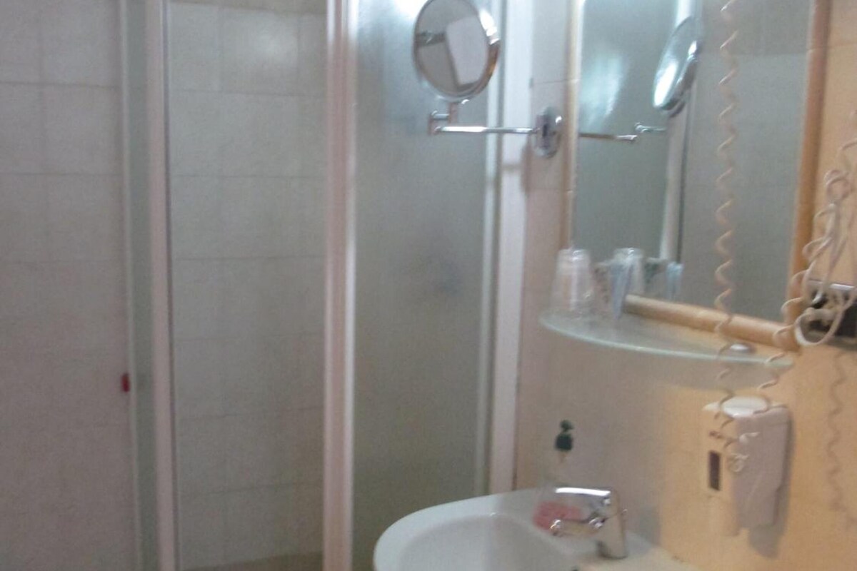 Un baño con ducha de mampara de vidrio, un lavamanos y un espejo.