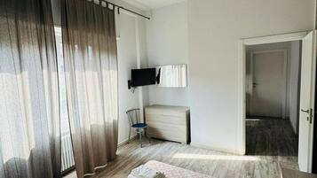 Una camera d'albergo con un letto, una sedia, una televisione e una porta che conduce in un'altra stanza.