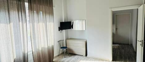 A hotel room with a bed, a chair, a television, and a door leading to another room.