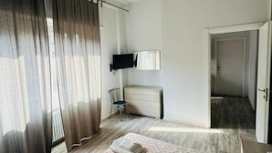 Una habitación de hotel con una cama, una silla, un televisor y una puerta que da a otra habitación.