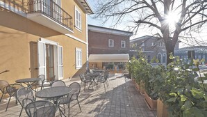 Un patio al aire libre con mesas y sillas, un edificio con balcón y un árbol.