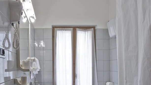 Baño con lavamanos, dos inodoros, cortina de ducha y ventana con cortinas.