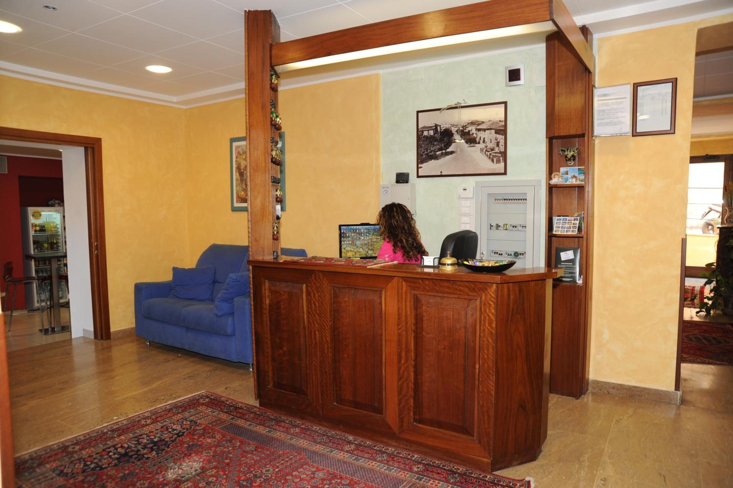 A reception area with a wooden reception desk, a blue sofa, a patterned rug, and a wall-mounted photo.