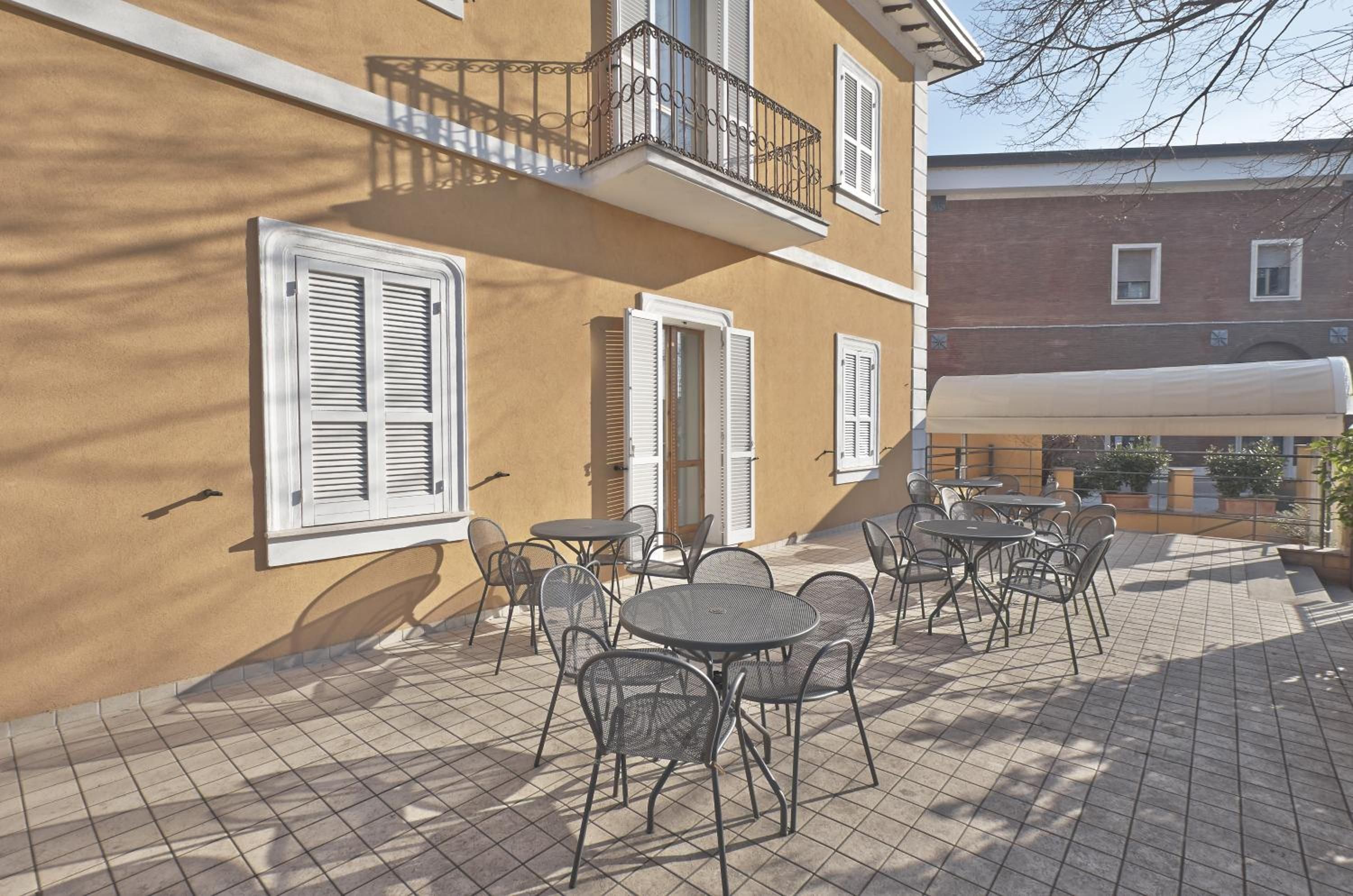 Una terrazza esterna con tavoli e sedie, un edificio con persiane e un tendone bianco.