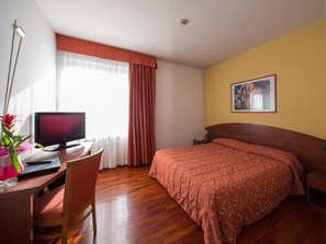 A hotel room with a bed, a desk with a computer, a chair, a window with curtains, and a painting on the wall. - Hotel La Cascata (Azzano San Paolo)