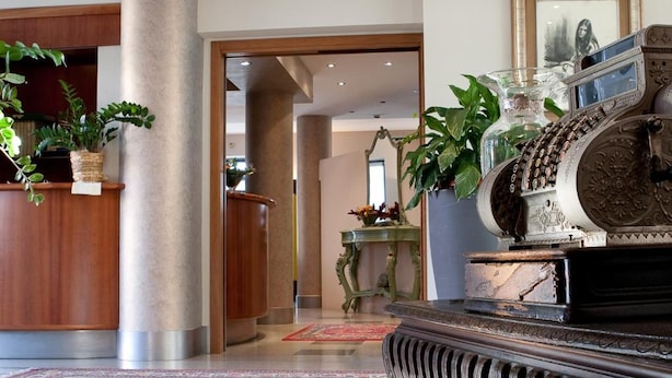 A lobby with a reception desk, a grand piano, and a large column. - Hotel La Cascata (Azzano San Paolo)