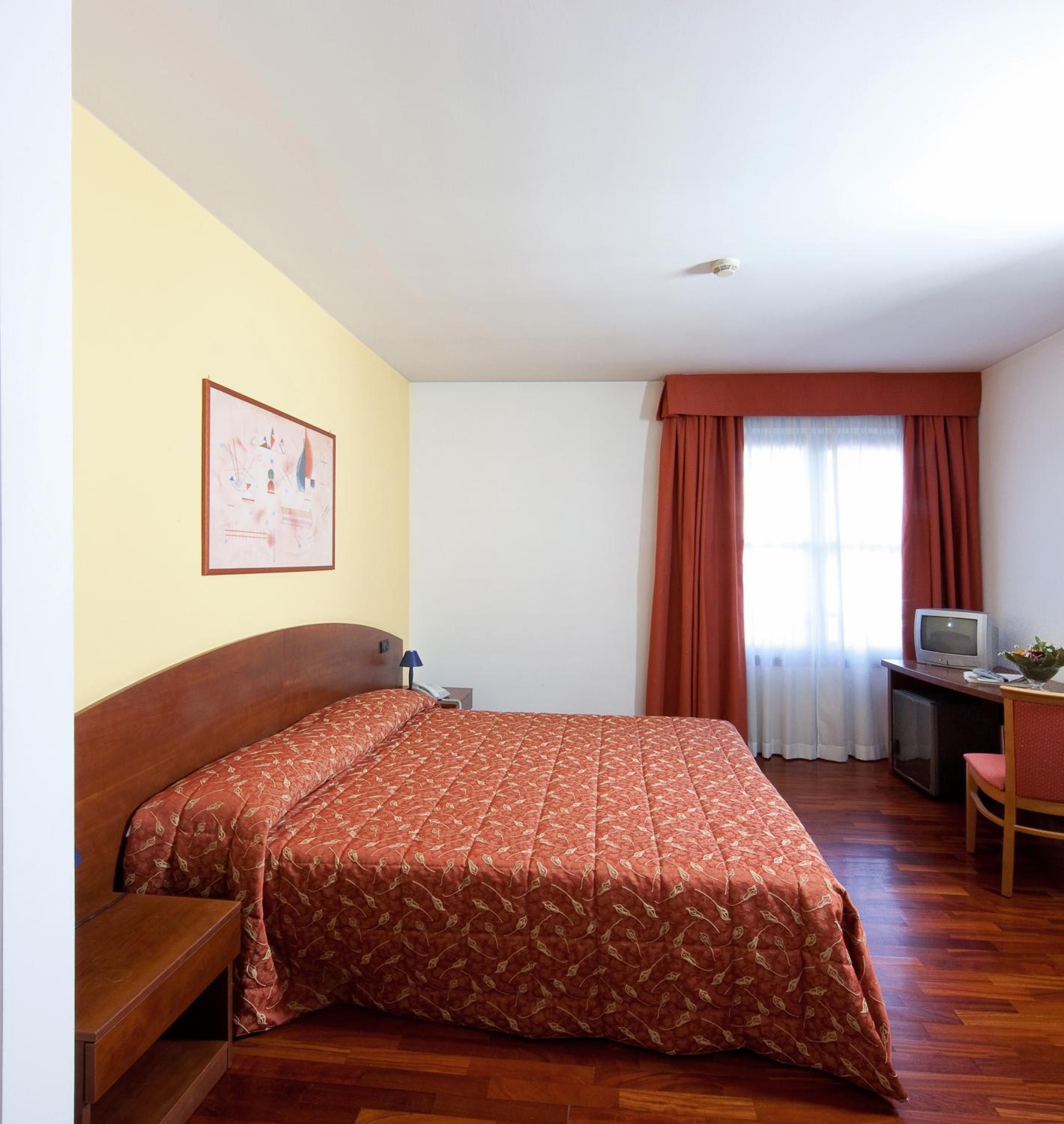 Una habitación de hotel con una cama, un escritorio con televisor y una silla.