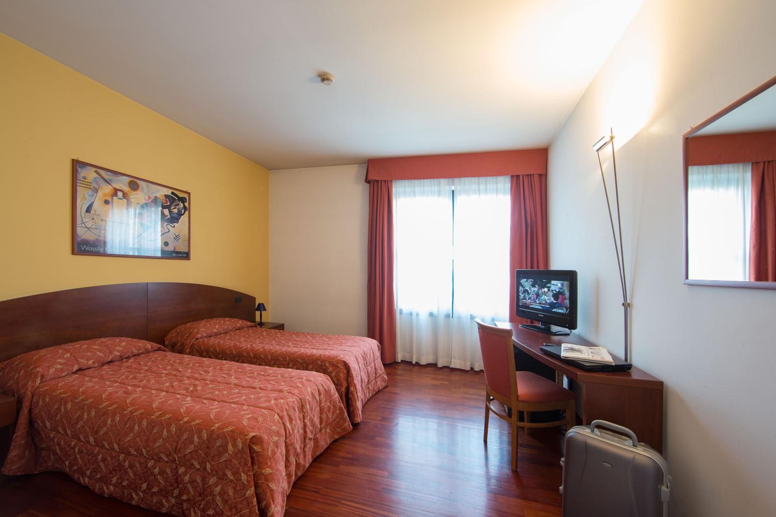A hotel room with two beds, a desk with a computer, a television, and a suitcase.