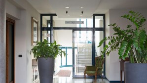 A hotel lobby with a large potted plant, a chair, and a carpeted floor. - Hotel La Cascata (Azzano San Paolo)