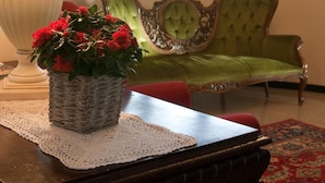A room with a lamp, a vase of flowers, a green upholstered sofa, and a chandelier. - Hotel La Cascata (Azzano San Paolo)