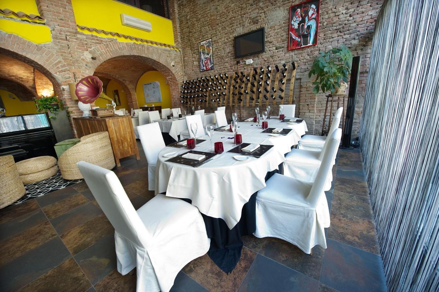 Ein Restaurant mit runden Tischen, weißen Stühlen und einer Backsteinwand mit Wandgemälde.