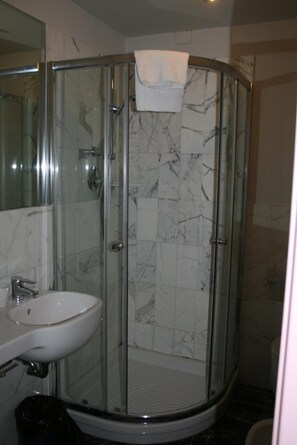 Ducha con paredes de vidrio, lavamanos blanco y azulejos de mármol.