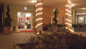 Entrada de hotel con alfombra roja, plantas en macetas y un cartel con un copo de nieve.