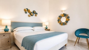 A neatly made bed with a blue throw, two bedside tables with lamps, a blue chair, and decorative wall art. - Hotel Guarracino (Capri)