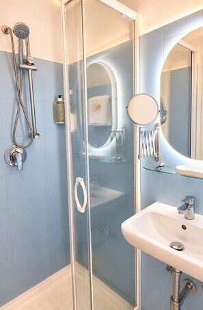 Un baño moderno con ducha envuelta en vidrio, un lavabo blanco con espejo y un estante de vidrio.