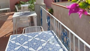 A terrace with a patterned table, white chairs, and a thatched roof. - Hotel Guarracino (Capri)