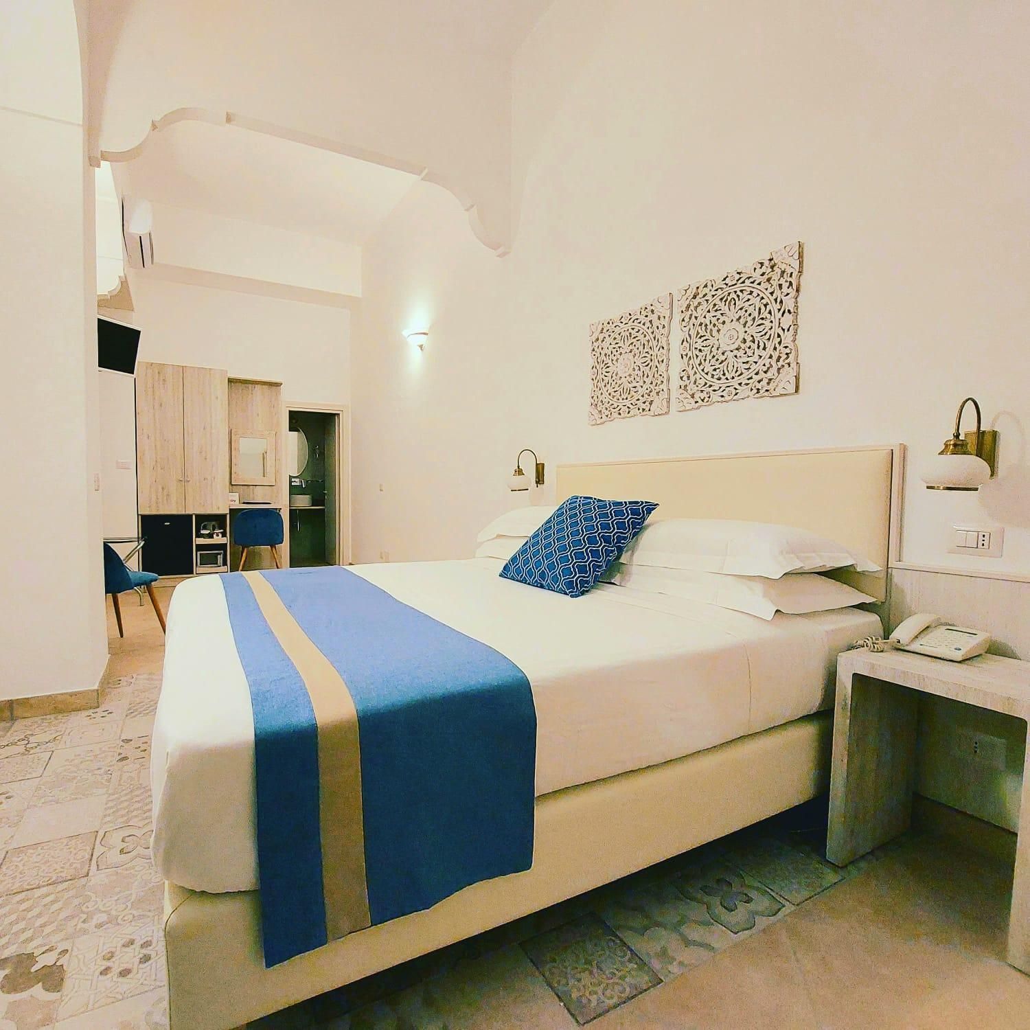 A hotel room with a bed, bedside table, lamp, and a desk with a telephone.