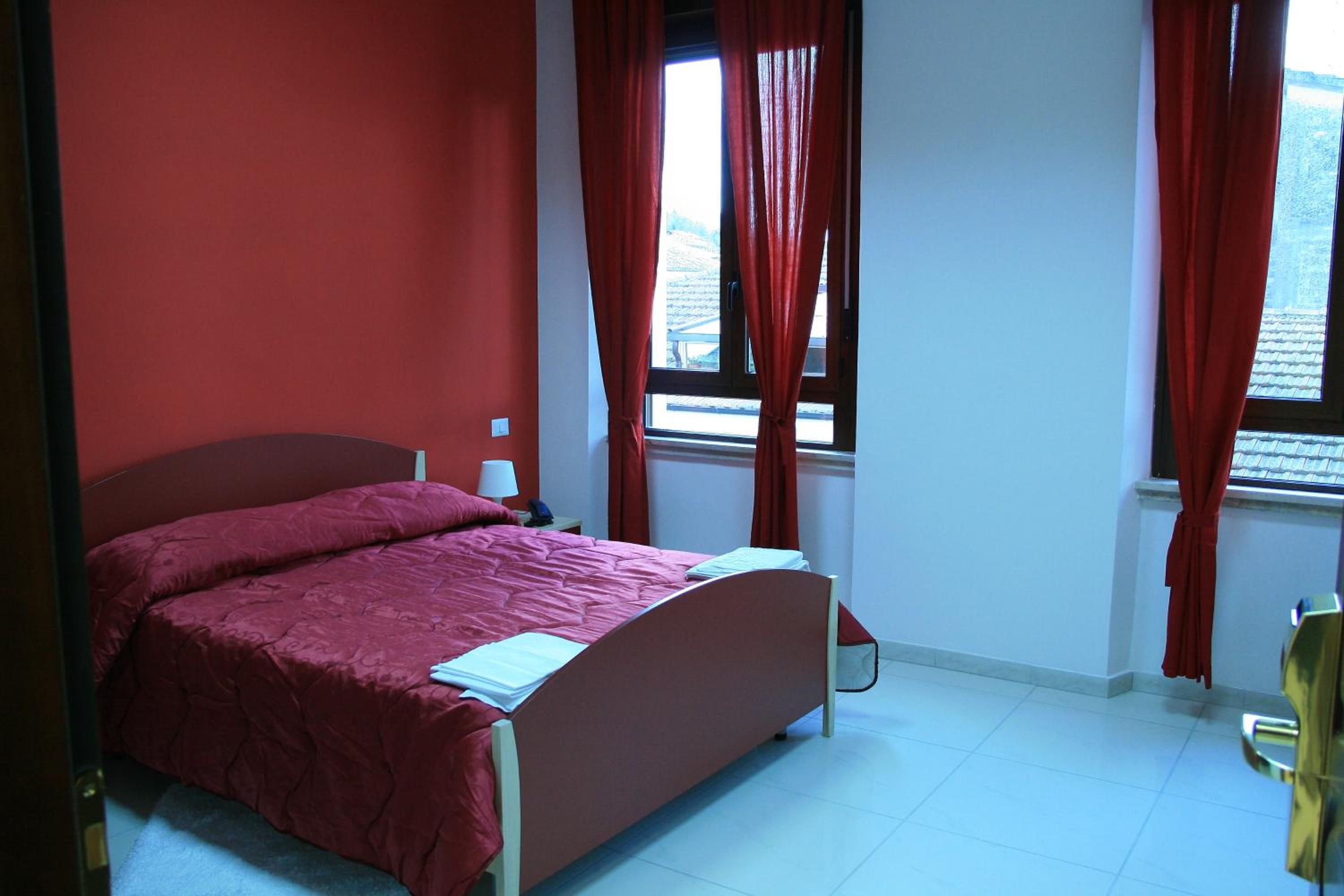 A bedroom with a bed, a nightstand, a lamp, and a window with curtains.