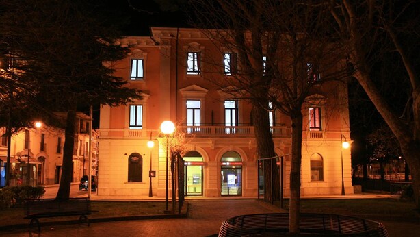 Ein historisches Gebäude mit einem zentralen Eingang, einem Innenhof mit Bänken und einer gut beleuchteten Fassade.