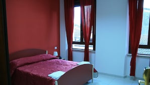 Ein Schlafzimmer mit Bett, Nachttisch, Lampe und einem Fenster mit Vorhängen.