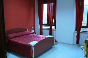 A bedroom with a bed, a nightstand, a lamp, and a window with curtains. - Albergo Ma.re (Popoli)