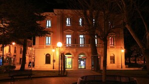 Un edificio histórico con una entrada central, un patio con bancos y una fachada bien iluminada.