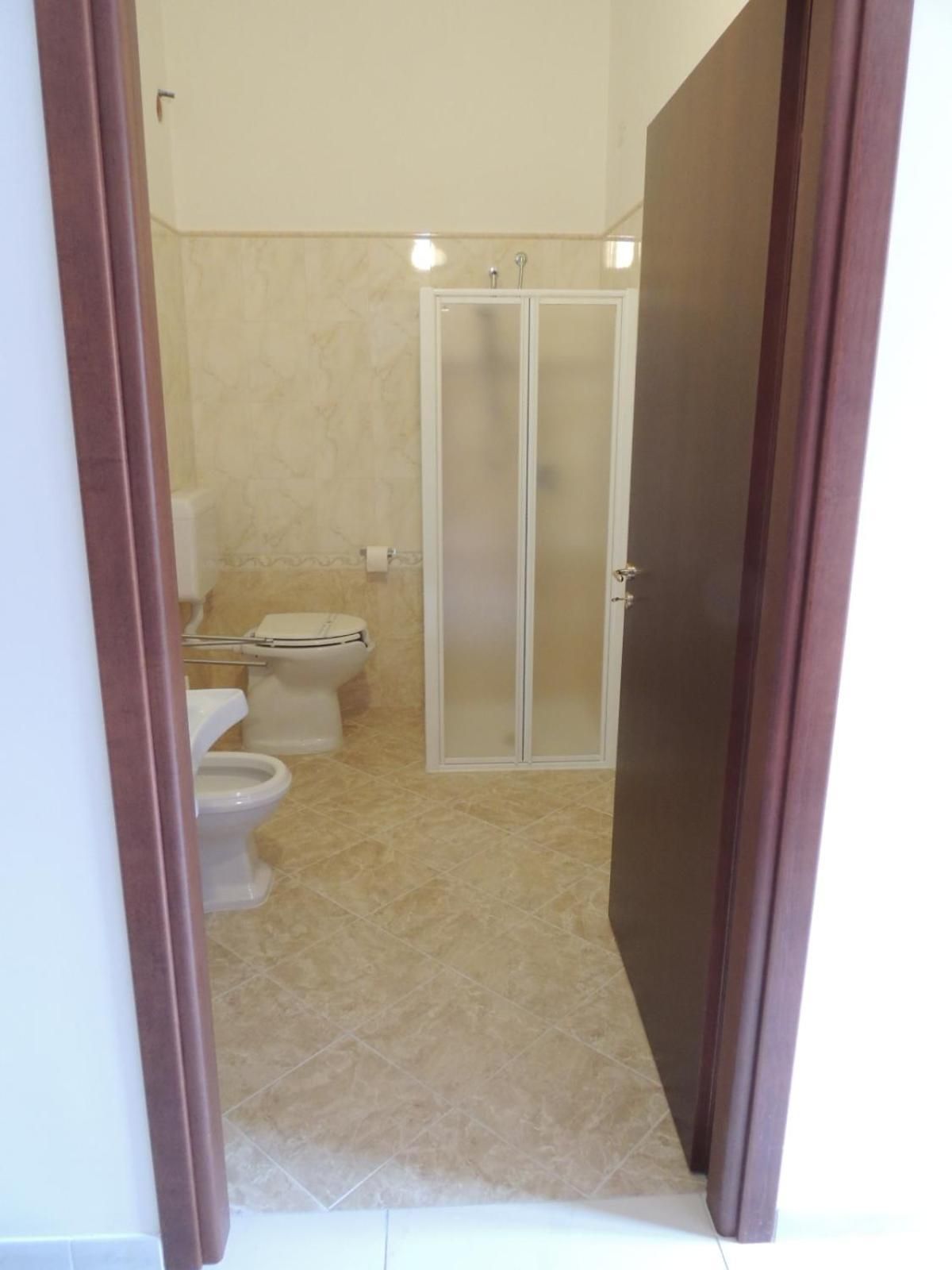 Baño con dos inodoros, cabina de ducha y suelo de baldosas.