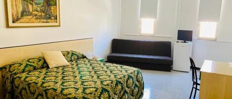 Una habitación con cama, escritorio, silla y televisor.