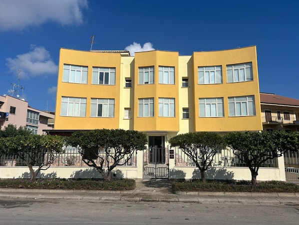 A yellow multi-story building with a symmetrical facade, large windows, and a gated entrance. - Franco Il Conte (Bagheria)