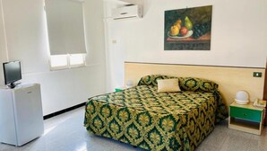 A hotel room with a bed, a small bedside table, a television, and a refrigerator. - Franco Il Conte (Bagheria)