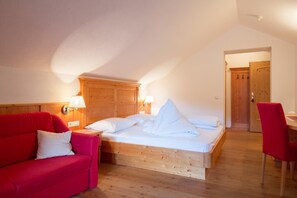 A bedroom with a wooden bed, a red sofa, a wooden door, and a wooden desk. - Frida Am Wald (Rasun Anterselva)