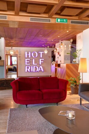 A hotel lobby with a red sofa, a reception desk, and a sign that reads 'HOTEL ELF RIDA.' - Frida Am Wald (Rasun Anterselva)