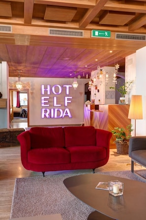 Un hall d'hôtel avec un canapé rouge, un comptoir de réception et une enseigne indiquant « HÔTEL ELF RIDA ».