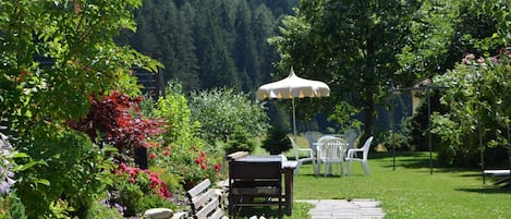 A garden with a stone pathway, a wooden bench, a table with chairs, and a white umbrella.