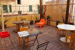 An outdoor patio area with a round wooden table, two chairs, a bench, and a small table with papers. - Albergo Delle Spezie (La Spezia)