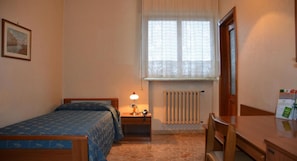 Un dormitorio con cama, mesita de noche, lámpara, radiador y una silla.