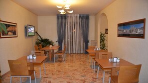 Habitación de hotel con comedor que incluye suelo de baldosas, mesas y sillas de madera, un televisor en la pared y cuadros enmarcados.