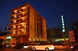 Un edificio de varios pisos con balcones, un semáforo y una señalización con indicaciones.