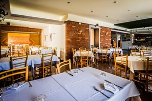 A restaurant with multiple tables and chairs, brick walls, and a bar area. - Al Vecchio Palazzo (Casto)