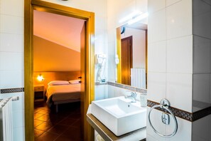 Una habitación de hotel con cama, mesita de noche, espejo, lavabo y toallero.