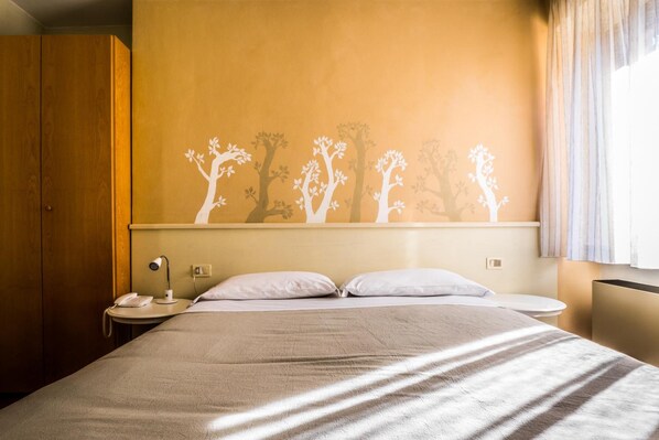 Una habitación de hotel con una cama, una mesita de noche, una lámpara y un muro con siluetas de árboles.