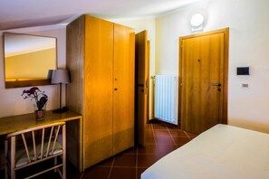 Habitación de hotel con cama, escritorio con lámpara, armario y espejo en la pared.