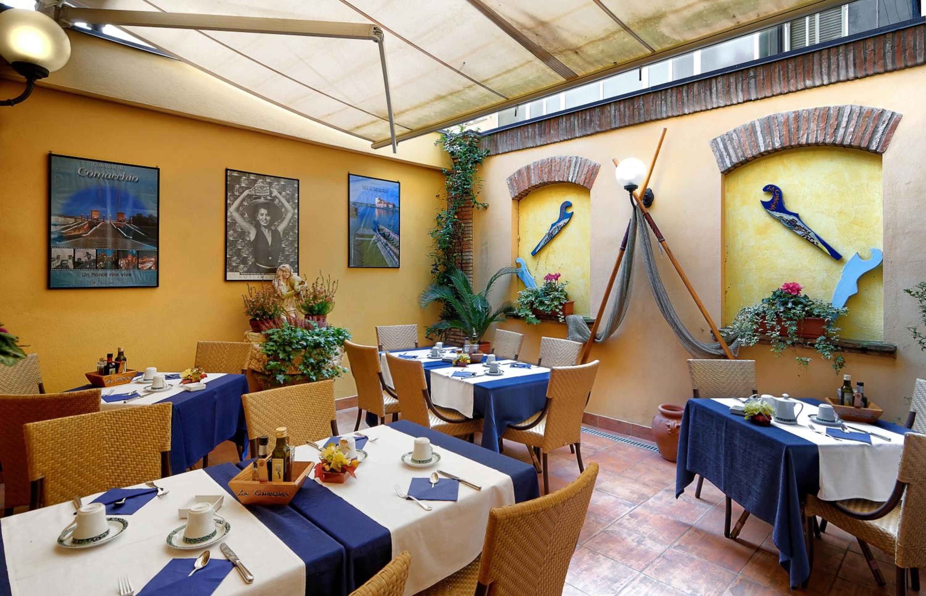 An outdoor dining area with tables set for two, covered with blue tablecloths, and surrounded by wicker chairs.
