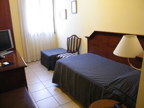 Una habitación de hotel con una cama, una silla, un escritorio con televisor y una lámpara.