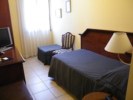 Una habitación de hotel con una cama, una silla, un escritorio con televisor y una lámpara.