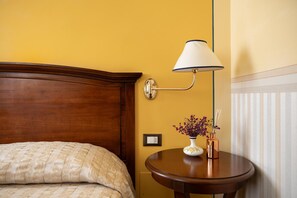 Una habitación de hotel con cabecera de madera, una mesita de noche con un jarrón de flores y una lámpara de pared.