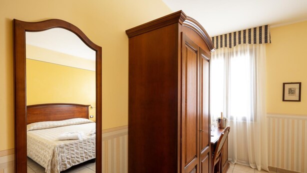 Habitación de hotel con un armario de madera, una cama con cubrecama blanco y un espejo grande que refleja la habitación.