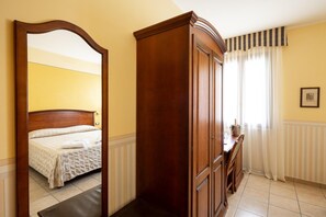 Habitación de hotel con un armario de madera, una cama con cubrecama blanco y un espejo grande que refleja la habitación.